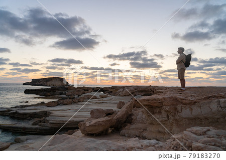 Male tourist with backpack watching beautiful view of Yeronisos Holy Island near coast Agios Georgios Pegeias In Cyprus on sunset. Man hiker looks into distance at deserted island in mediterranean sea Male tourist with backpack watching beautiful view of Yeronisos Holy Island near coast Agios Georgios Pegeias In Cyprus on sunset. Man hiker looks into distance at deserted island in mediterranean sea 79183270