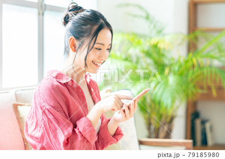 ソファでくつろぎながらスマホを操作する女性。 ソファでくつろぎながらスマホを操作する女性。 79185980