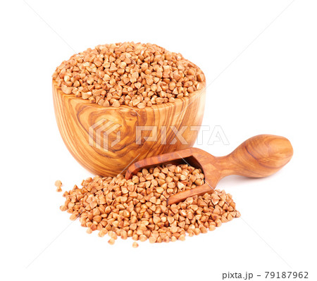 Roasted buckwheat grains in olive bowl and scoop, isolated on white background. Dry brown buckwheat groats. 79187962