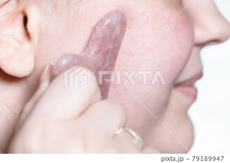 massaging female cheek with quartz scraper closeup 79189947