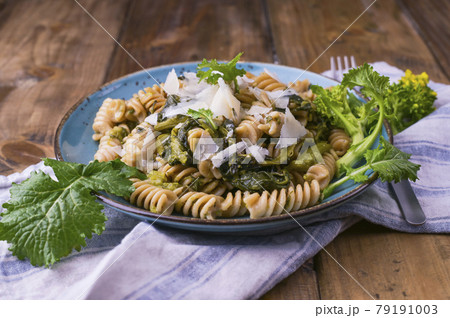 Cime di rapa pasta in a plate on with parmesan on a wooden table. Cime di rapa pasta in a plate on with parmesan on a wooden table. 79191003