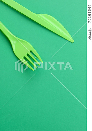 Disposable plastic cutlery green. Plastic fork and knife lie on a green background surface Disposable plastic cutlery green. Plastic fork and knife lie on a green background surface 79191644