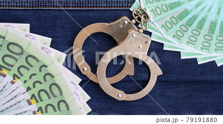 The fan of a lot of euro bills and police handcuffs is on a dark denim surface. Background image 79191880