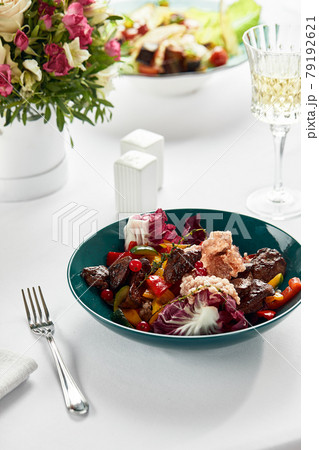Veal liver with salad and mango and orange slices, raman leaves, frieze and red berries, close-up, light background, white dishes, creative serving of veal liver 79192621