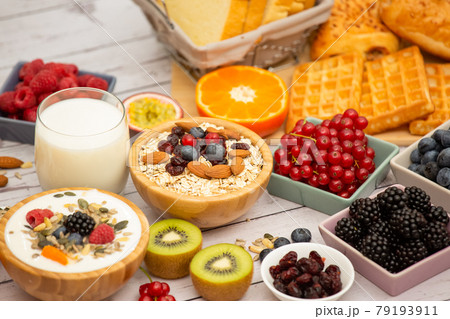 Breakfast Served in the morning with Butter bread and corn flakes Whole grains and raisins with milk in cups and Strawberry, Blueberry, Raspberry, Kiwi, Fresh Orange  on the breakfast table. 79193911