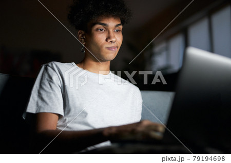 Night portrait of young guy looking at the screen, working on laptop in dark room, sitting on a couch at home 79194698