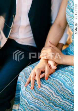 Man in a suit and woman in a striped blue dress are sitting holding hands 79197008