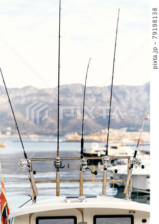 Fishing rods attached to the stern of a white yacht against the backdrop of a pier, boats, sea and mountains. Close-up 79198138
