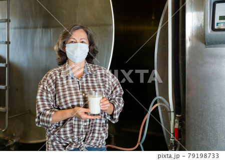 Mature woman in protective mask is holding glass of milk at cow farm Mature woman in protective mask is holding glass of milk at cow farm 79198733