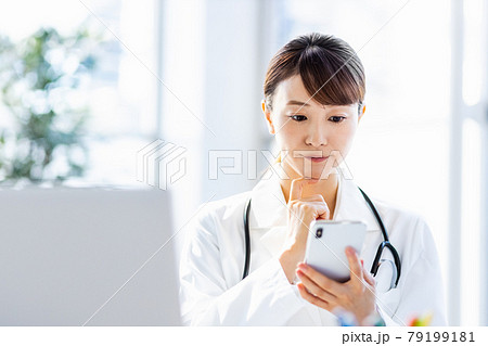 病院内でスマートフォンを見ている女性医師 病院内でスマートフォンを見ている女性医師 79199181