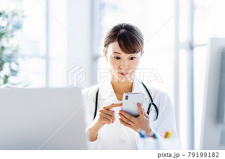 病院内でスマートフォンを見ている女性医師 病院内でスマートフォンを見ている女性医師 79199182