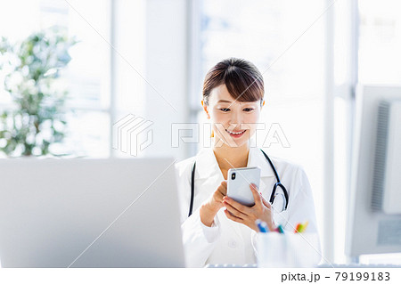 病院内でスマートフォンを見ている女性医師 病院内でスマートフォンを見ている女性医師 79199183
