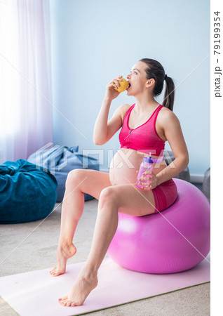 Faceless pregnant woman eating an apple after yoga. Expectant mother bites fruit and drinks water after Pilates. Girl sitting on a fitness ball. Faceless pregnant woman eating an apple after yoga. Expectant mother bites fruit and drinks water after Pilates. Girl sitting on a fitness ball. 79199354