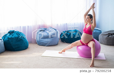 Beautiful pregnant woman doing exercises on a fitness ball. Expectant mother in the last trimester doing yoga. 79200258