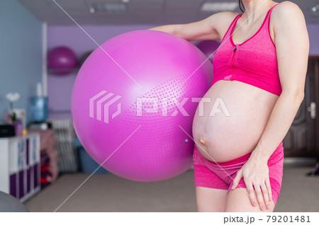 Cropped view of unrecognizable pregnant woman in yoga class. Future mother faceless with a bare tummy is engaged in fitness with a ball. 79201481