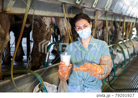 Portrait of female dairy farm worker in protective mask standing with glass of milk 79201927