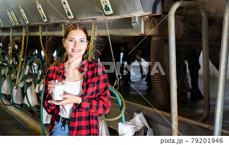 Female milker posing with glass of milk on dairy farm Female milker posing with glass of milk on dairy farm 79201946
