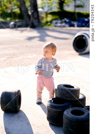 Kid stands near the piled up car tires in the parking lot 79204343