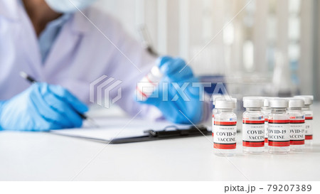 Covid-19 coronavirus vaccine bottles on white table with scientist working in pharmaceutical research laboratory background. Fight against Covid-19 coronavirus Concept. Covid-19 coronavirus vaccine bottles on white table with scientist working in pharmaceutical research laboratory background. Fight against Covid-19 coronavirus Concept. 79207389
