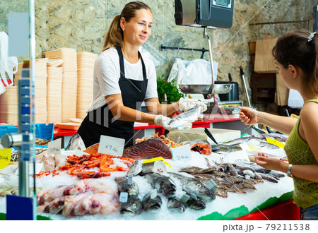 saleswoman offering fresh whole sea bass to buyer 79211538