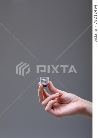 Close up of caucasian businesswoman holding base of light bulb, isolated on grey background 79212494