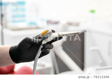 The gloved hand of the dentist holds the Airflow whitening and cleaning brush to remove tartar and plaque. 79213306