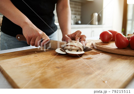 Close-up of chef or housewife hands while slicing mushrooms on a wooden kitchen board 79215511