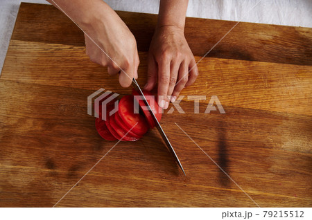 Top view of woman hand cutting tomato on a wooden board Top view of woman hand cutting tomato on a wooden board 79215512