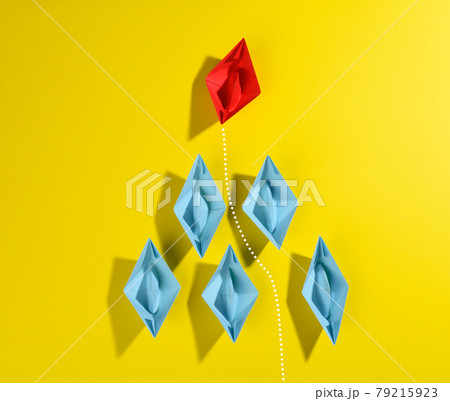group of blue paper boats and one red led on a yellow background. group of blue paper boats and one red led on a yellow background. 79215923
