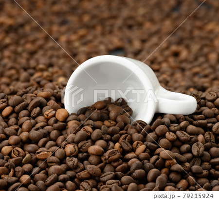 white ceramic cup lies on a pile of brown roasted arabica and robusta coffee beans white ceramic cup lies on a pile of brown roasted arabica and robusta coffee beans 79215924