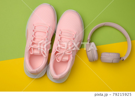 pair of pink sneakers, wireless headphones on a yellow background pair of pink sneakers, wireless headphones on a yellow background 79215925
