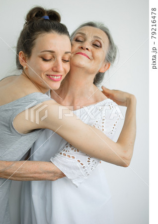 Happy senior mother is hugging her adult daughter, the women are laughing together, sincere family of different age generations having fun on white background Happy senior mother is hugging her adult daughter, the women are laughing together, sincere family of different age generations having fun on white background 79216478