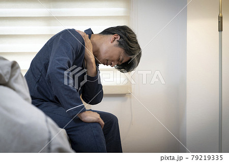ベッドに座って肩を手で押える中高年男性 79219335