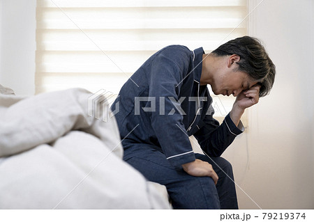 ベッドに座って頭を抱える50代の男性 79219374