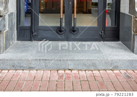 a threshold with a step at the threshold entrance to the store with a black iron door with glass insert in the doorway tile with gray granite close-up front view, nobody. a threshold with a step at the threshold entrance to the store with a black iron door with glass insert in the doorway tile with gray granite close-up front view, nobody. 79221283