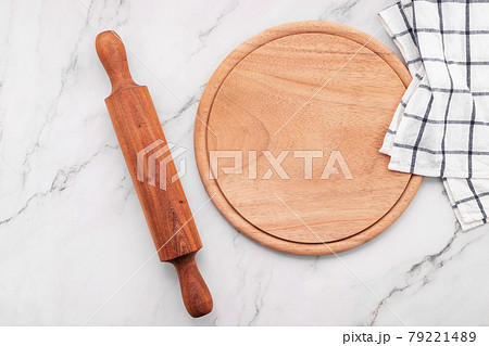 Empty wooden pizza platter with napkin and rolling pin set up on marble stone kitchen table. Pizza board and tablecloth on white marble background. 79221489