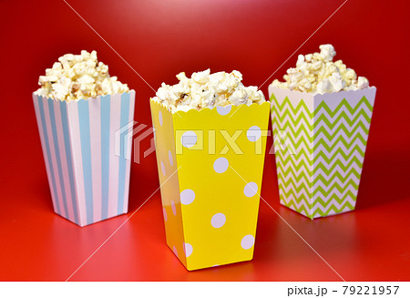Popcorn in colored cardboard packaging. Heap of salted popcorn in paper striped bucketon on red  79221957