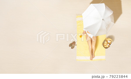 Alone woman in bikini sitting and sunbathes on yellow beach towel under umbrella with bag and juice. Female relaxation on the sand beach at summer vacation. Top, aerial view Alone woman in bikini sitting and sunbathes on yellow beach towel under umbrella with bag and juice. Female relaxation on the sand beach at summer vacation. Top, aerial view 79223844