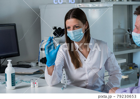 Close-up of coronavirus vaccine jar in female Caucasian hand with blurred face of serious middle aged woman at background. Close-up of coronavirus vaccine jar in female Caucasian hand with blurred face of serious middle aged woman at background. 79230653