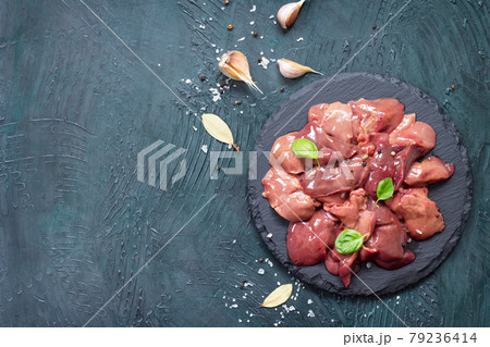 Raw chicken liver on a slate board and spices a gray stone background. Top view with copy space. 79236414