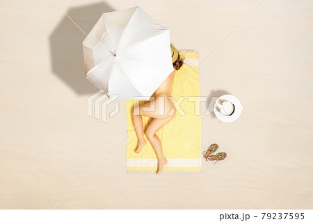 Alone naked woman in straw hat lying and sleeping on yellow beach towel under beach umbrella. Female relaxation on the sand beach at summer vacation. Top, aerial view 79237595