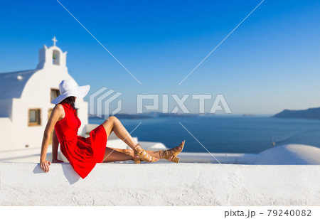 Santorini travel tourist brunette woman in red dress visiting famous white Oia village. Santorini travel tourist brunette woman in red dress visiting famous white Oia village. 79240082