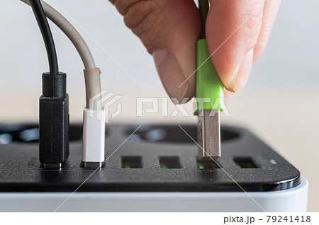 Modern convenient multi-port usb charger for devices. Close-up of a female hand plugging multi-colored cables into a power outlet. Macro. 79241418