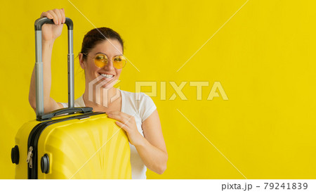 Smiling woman in sunglasses holding suitcase with retractable handle on yellow background 79241839