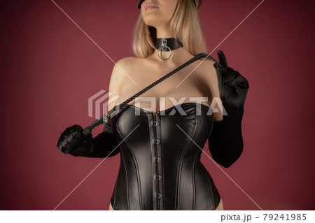 Beautiful young woman in a leather corset posing with a whip in her hands 79241985