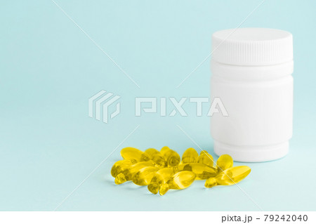Fish oil yellow supplement capsules omega-3 isolated and white plastic container bottle on blue surface. Health care concept Fish oil yellow supplement capsules omega-3 isolated and white plastic container bottle on blue surface. Health care concept 79242040