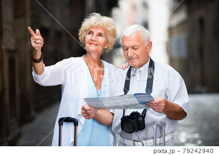 Senior couple of tourists with map and city guide walking 79242940