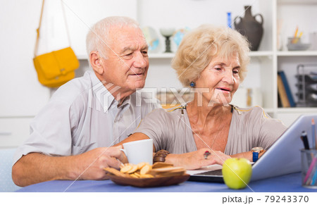 Cheerful mature spouses using laptop at home 79243370