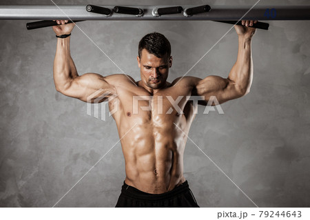 Fitness in gym, sport and healthy lifestyle concept. Handsome athletic man with naked torso making exercises. Bodybuilder male model pumping up muscles making pulls up on the crossbar. Front view Fitness in gym, sport and healthy lifestyle concept. Handsome athletic man with naked torso making exercises. Bodybuilder male model pumping up muscles making pulls up on the crossbar. Front view 79244643