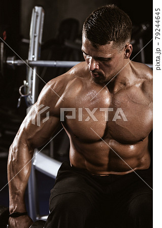 Fitness in gym, sport and healthy lifestyle concept. Handsome athletic man with naked torso making exercises. Bodybuilder male model trains deltoid muscles with dumbbells. Heavy barbell on background 79244645